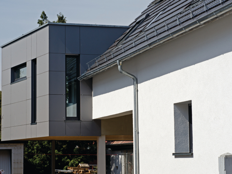 Ein modernes Haus mit einer Mischung aus glatten weißen und grauen Fassaden, großen Fenstern und einem Dach mit Metallblechen.