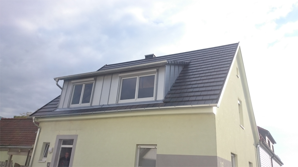 Ein gelbes Einfamilienhaus mit einem Dachfenster und einem dunklen Dach unter einem bewölkten Himmel.
