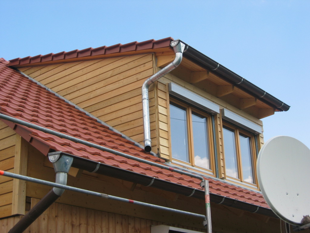 Dachansicht eines Hauses mit roten Ziegeln, Holzfassade, Fenstern und Regenrinnen.