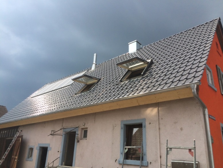 Ein Haus mit einem Dach, zwei Dachfenstern, einer orangefarbenen Wand und einer Treppe im Vordergrund.
